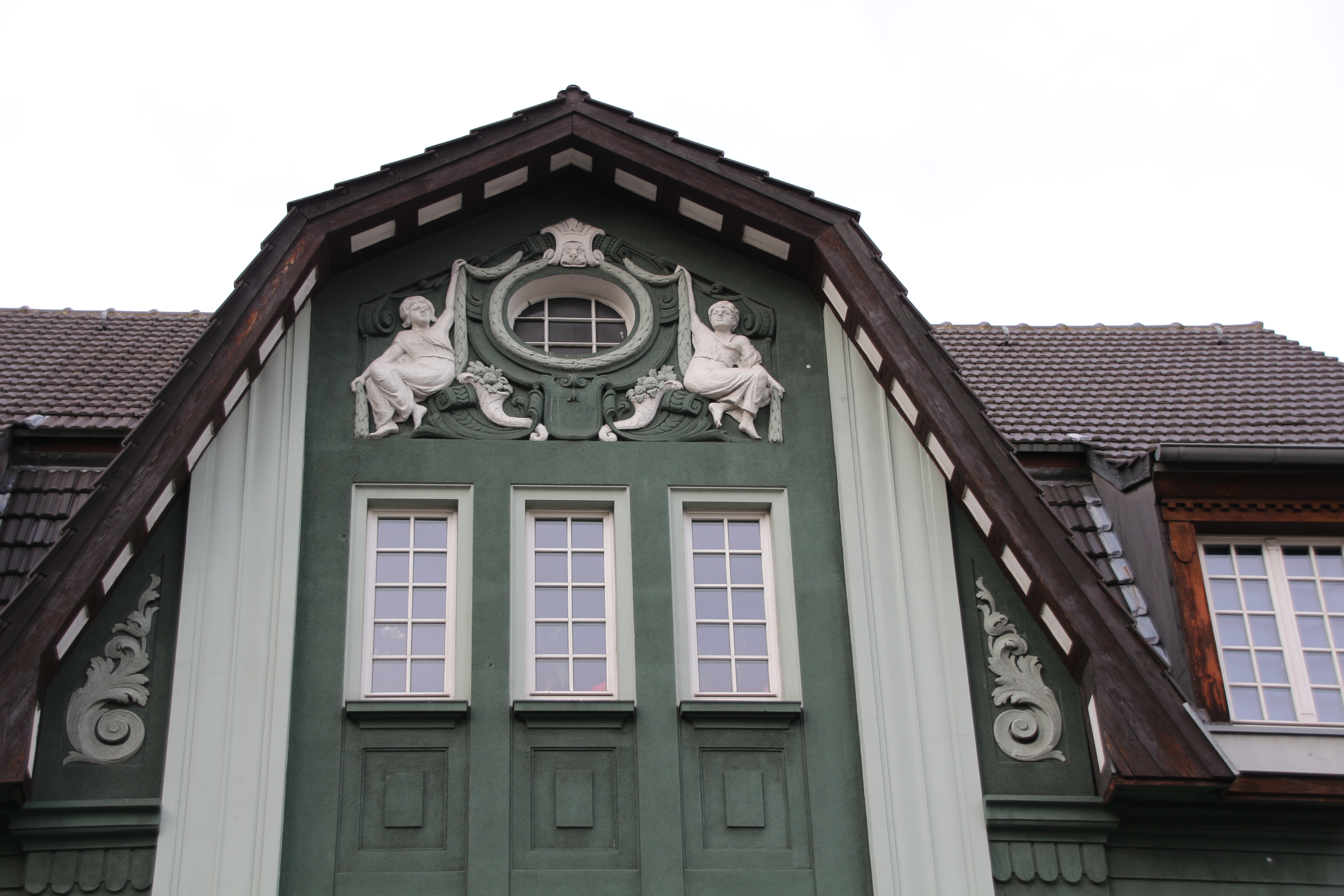 Rundfenster mit reliefierten, auf Voluten (Spiralen) sitzenden Frauengestalten